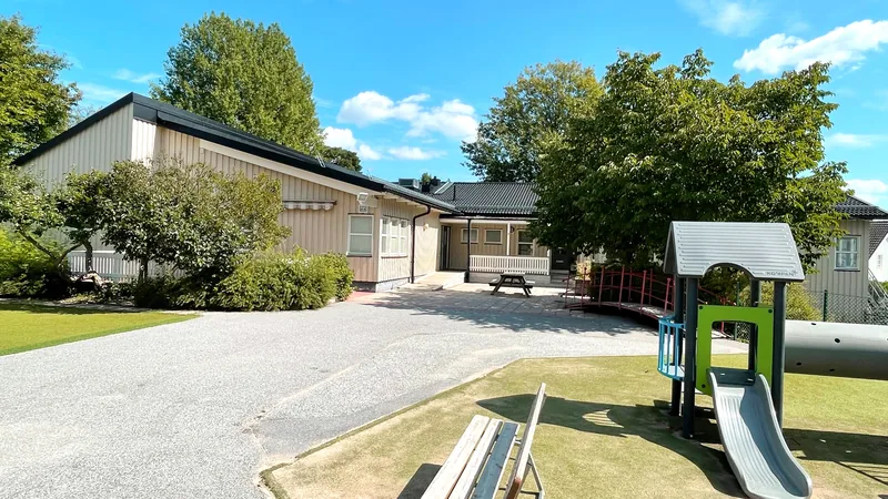 Bild av hus med lekplats, träd, gräsmatta och asfalt utanför på gården.