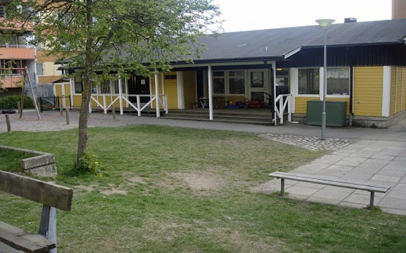 Gul förskola med lekplats framför och höghus bredvid.