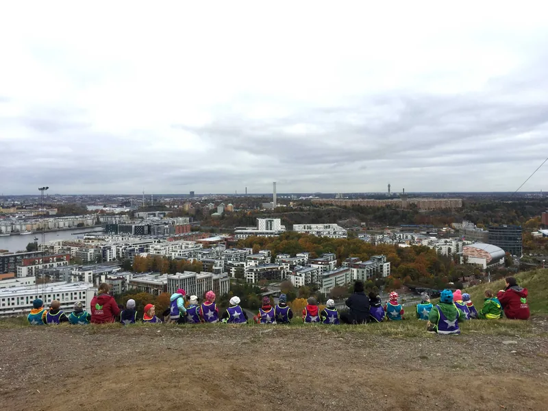 Barn och pedagoger sitter på ett berg och tittar på utsikten