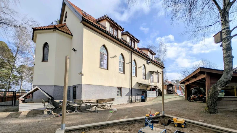 Hus med lekyta framför - bland annat en sandlåda, sittplatser och rutschkana.