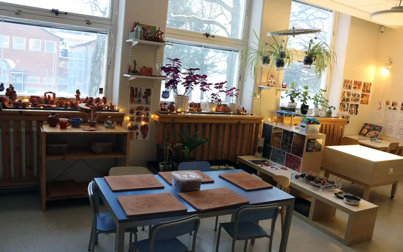 Interiör från förskolan med arbetsbord, låga hyllor och tända ljusslingor.