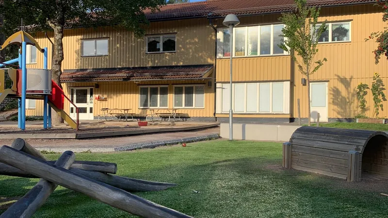 Gul träbyggnad med lekytor och gräsmatta.