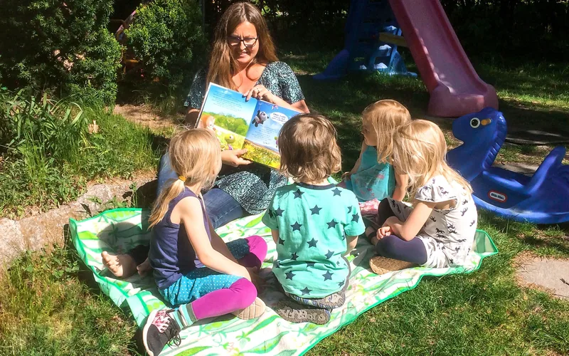 Barn och pedagog sitter på en filt, tittar i en bok.