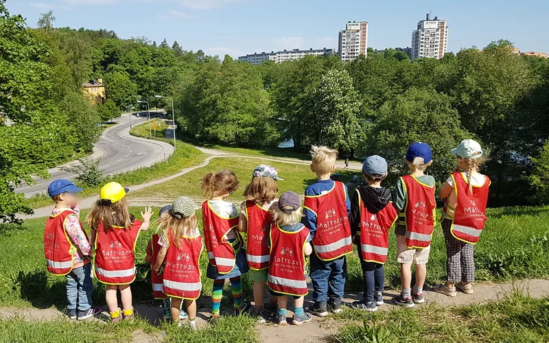 En grupp barn i förskolans västar står på en höjd och ser ut över staden.