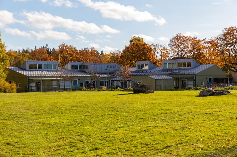 Byggnad med skog i bagrunden och ett öppet fält utanför gården till byggnaden