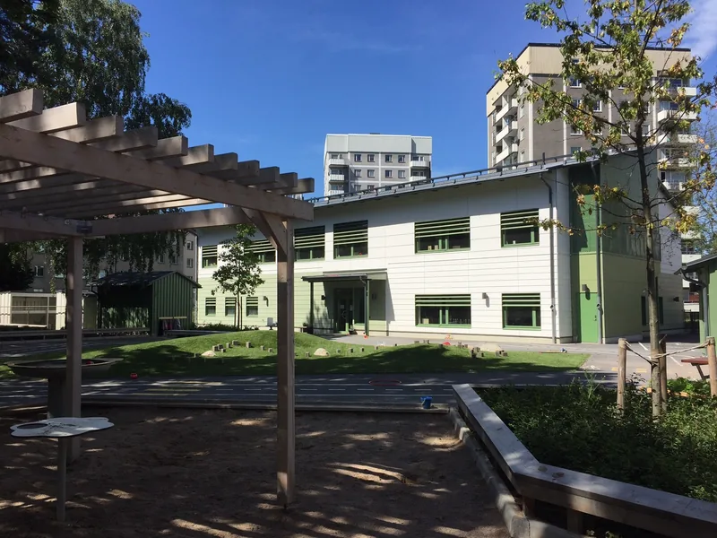 En solig tvåvåningsbyggnad med sandlåda och en pergola på gården
