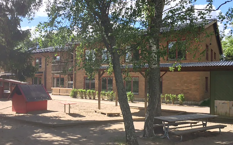 Bild på förskolans tegelfasad samt stora och lummiga förskolegård som inbjuder till aktiva lekar.