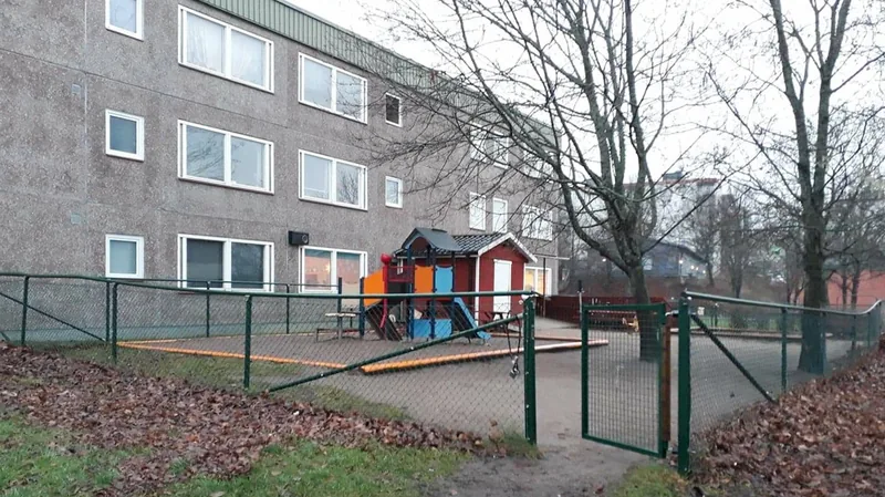 En inhägnad lekplats med rutschkana och sandlåda.
