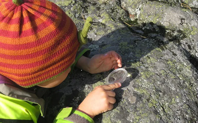 Ett barn ligger på ett berg och tittar genom ett förstoringsglas