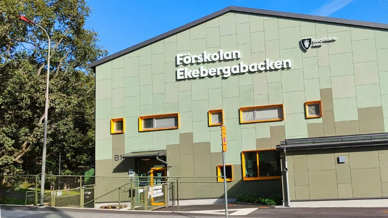 Fasaden på förskolan. Väggarna är ljust turkosa med texten "Förskolan Ekebergabacken" på. Till höger ser man träd och växtlighet från förskolans utegård. Foto.