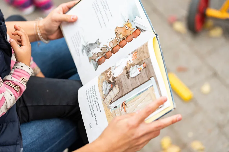 Barn sittandes i pedagogs knä med en bok uppslagen