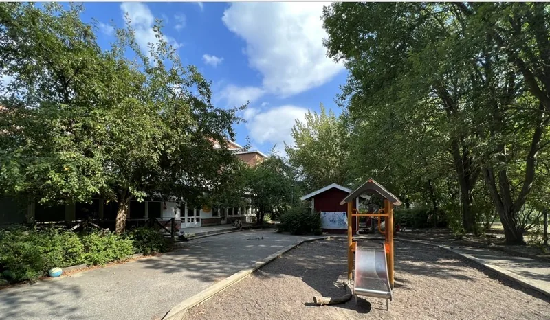 En förskolegård med en sandlåda och en liten rutschkana.