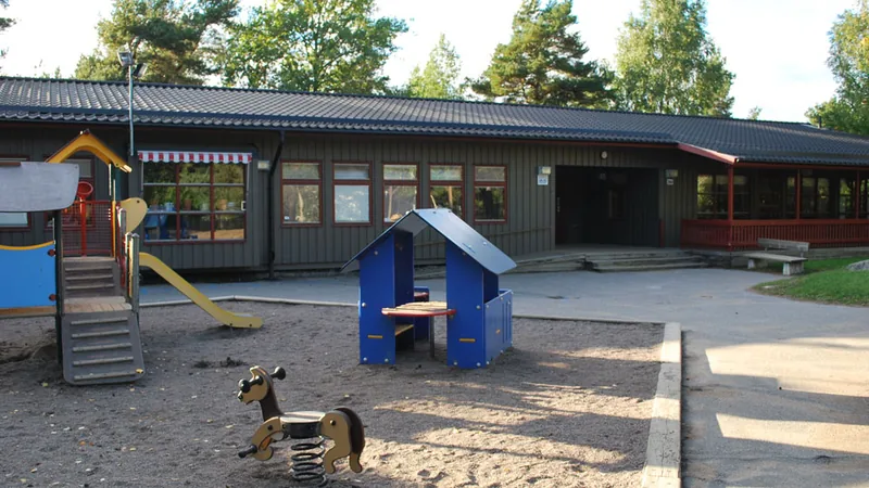 Förskolegården med lek och klätterställning i förgrunden.