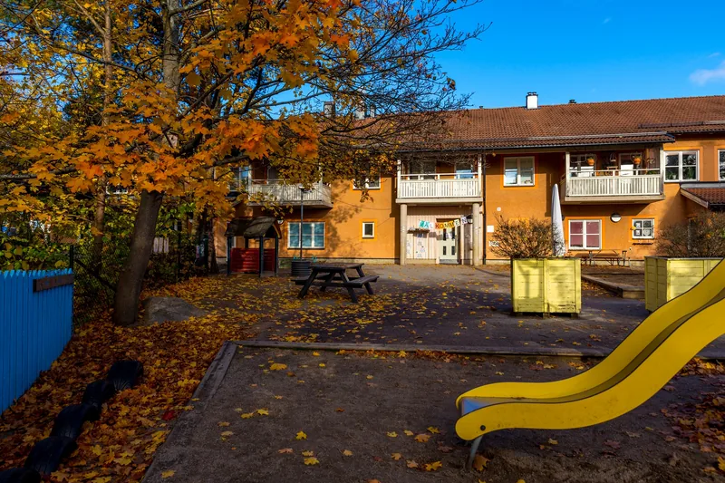 Gård med ruschkana, sandlåda och träd med byggnad i bakgrunden.