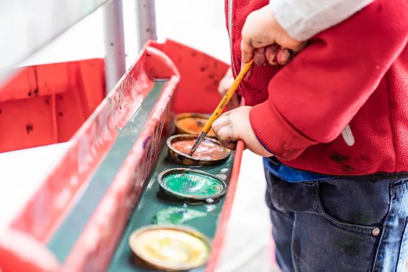 Barn som står vid målar färg och doppar en pensel