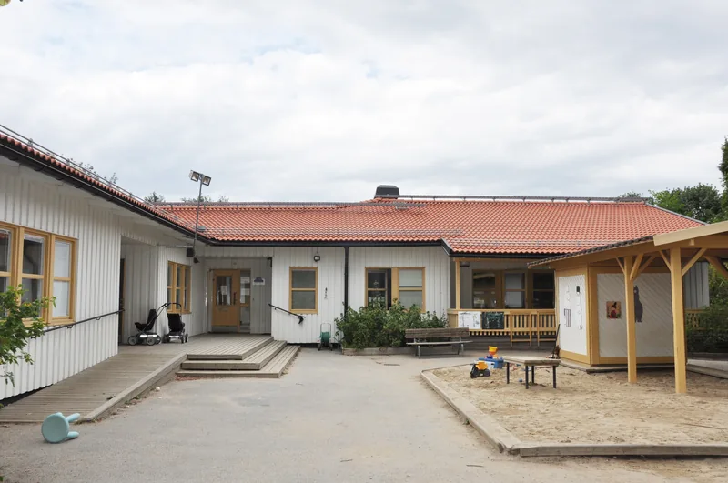 Stor ljus gård med sandlåda och ett ljust enplans hus i trä.