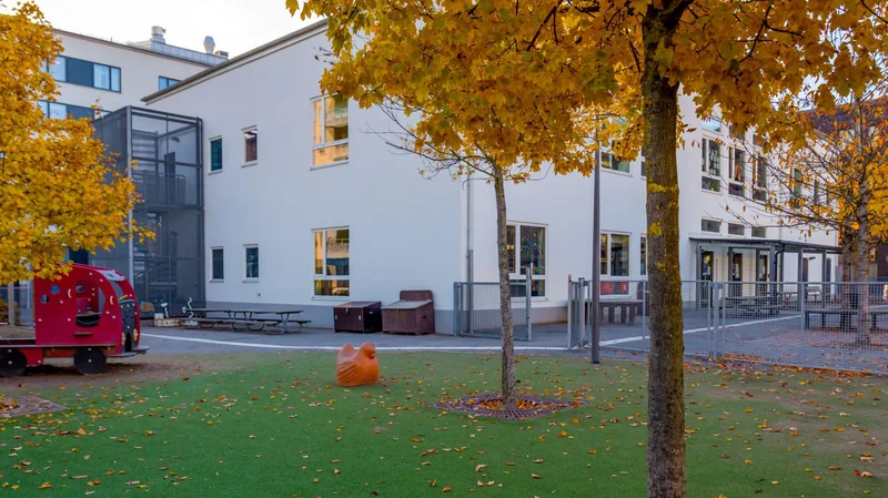 Förskolan Pippi Långstrumps gata 12. Framför syns en grön gräsmatta och träd med höstgula löv.
