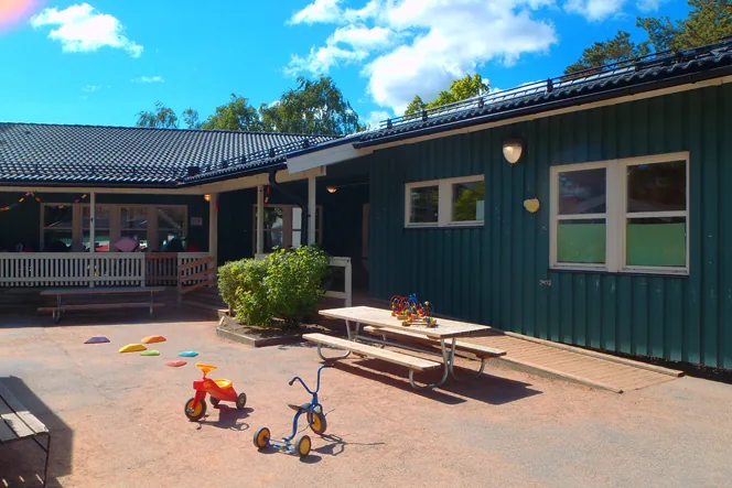 Ett grönt hus i vinkel, en gård med sandleksaker och leksakscyklar.