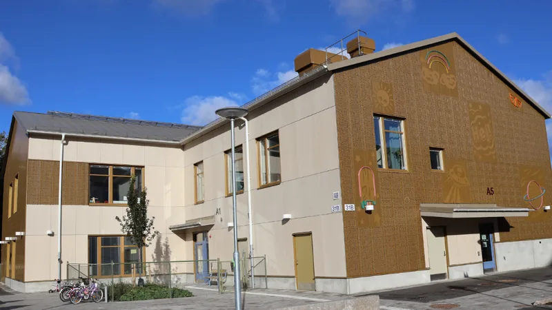Förskolans fasad. Ena sidan har en guld-beige färg med ljusinstallationer med rymdtema; en sol, en planet, ett ufo. Foto.