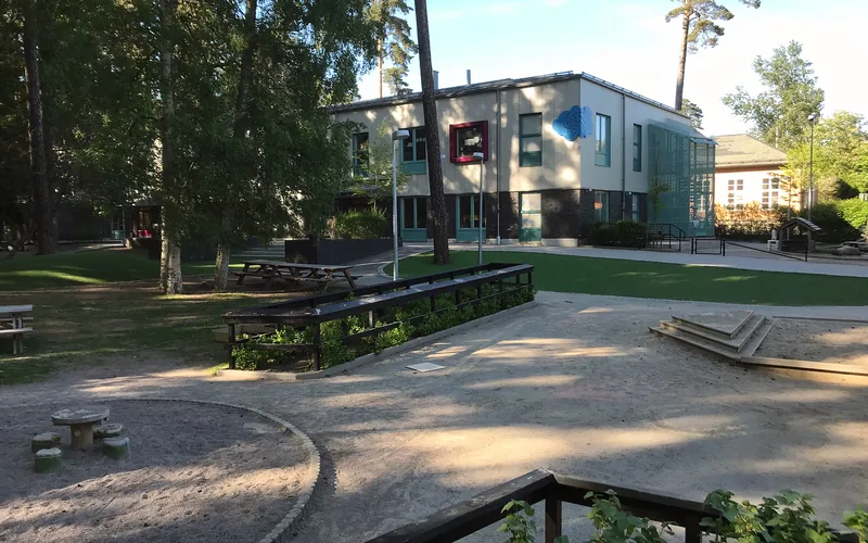 Förskolegården med lekredskap, sandlåda och grönytor och med förskolebyggnaden i bakgrunden..