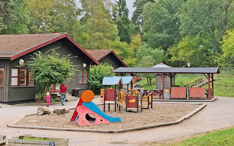 Förskolegård med rutschkana, sandlåda och andra lekmöbler.