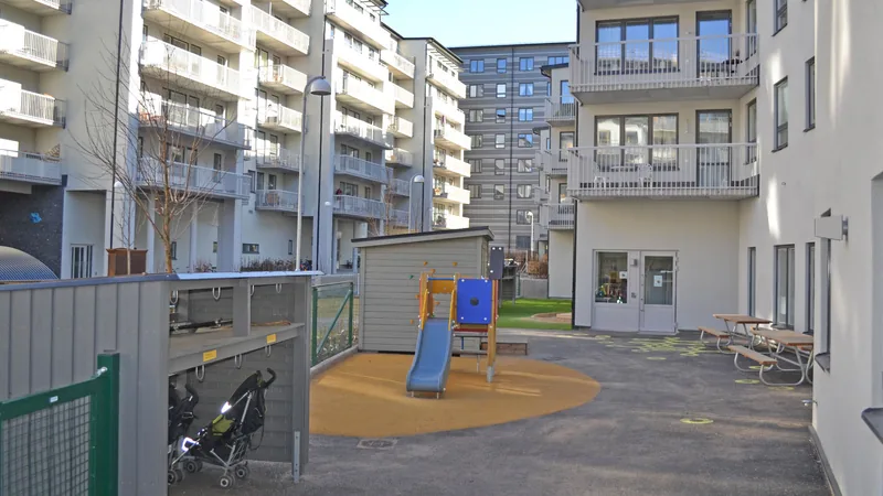 Utemiljö med lekytor och klätterställning och rutchkana. Vita flerbostadshus runtom gården.