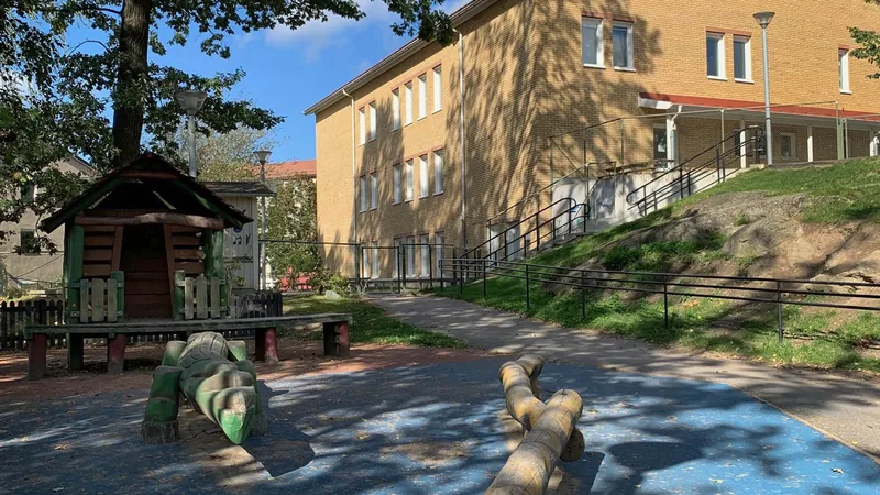 Utemiljö med lekplats och gul tegelbyggnad i tre plan i bakgrunden.