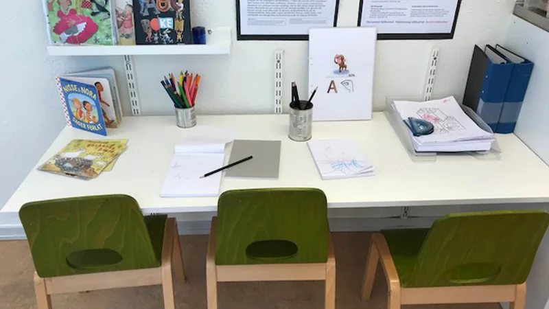 Innemiljö med ljusa väggar, bord, gröna stolar och olika lärande material.