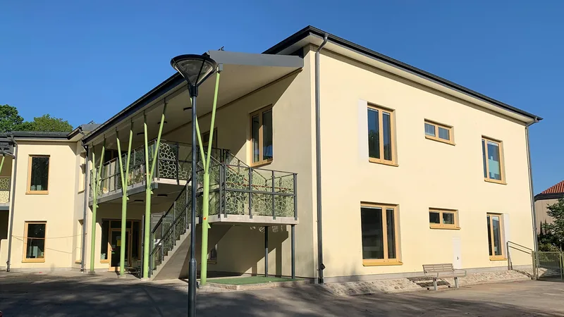 Ljusgul byggnad i två plan och stora trappor längs fasaden.