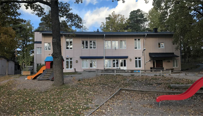 Utsidan av en förskola med lekplats, rutschkana och klätterställning, höstlöv på marken.