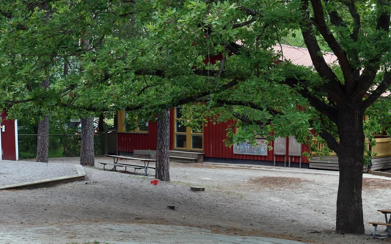Del av förskolegården med träd i förgrunden och förskolehuset i bakgrunden.