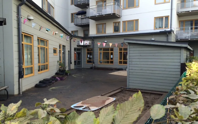 Utemiljö med lekytor och sandlåda. Vitt flerbostadshus i bakgrunden.