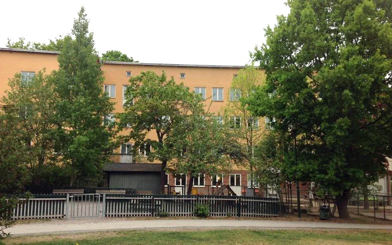Flerbostadshus med gul fasad med förskolegård i förgrunden.