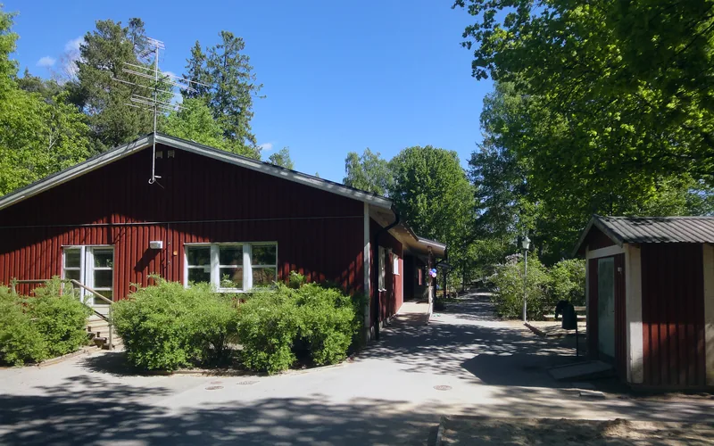 Ingången till förskolegården med husets röda gavel och buskar i fokus.