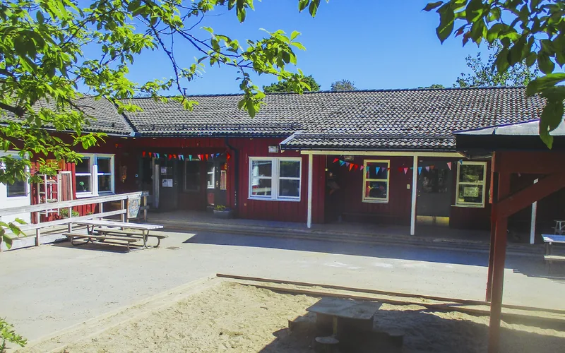 Röd enplansbyggnad med sandlåda i förgrunden.